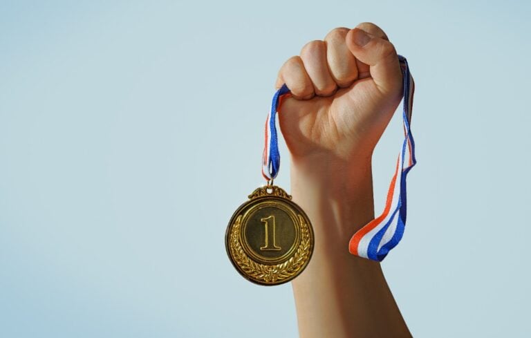woman hand raised, holding gold medal against sky. award and victory concept