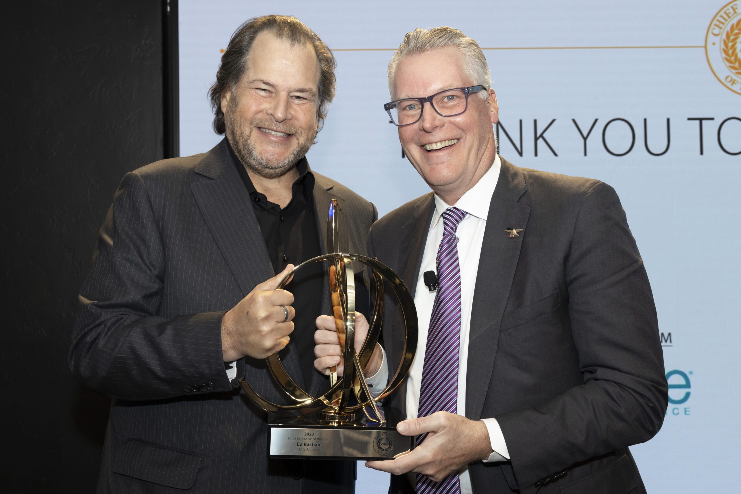 Marc Benioff and Ed Bastian smiling and holding a large, gold, spherical award