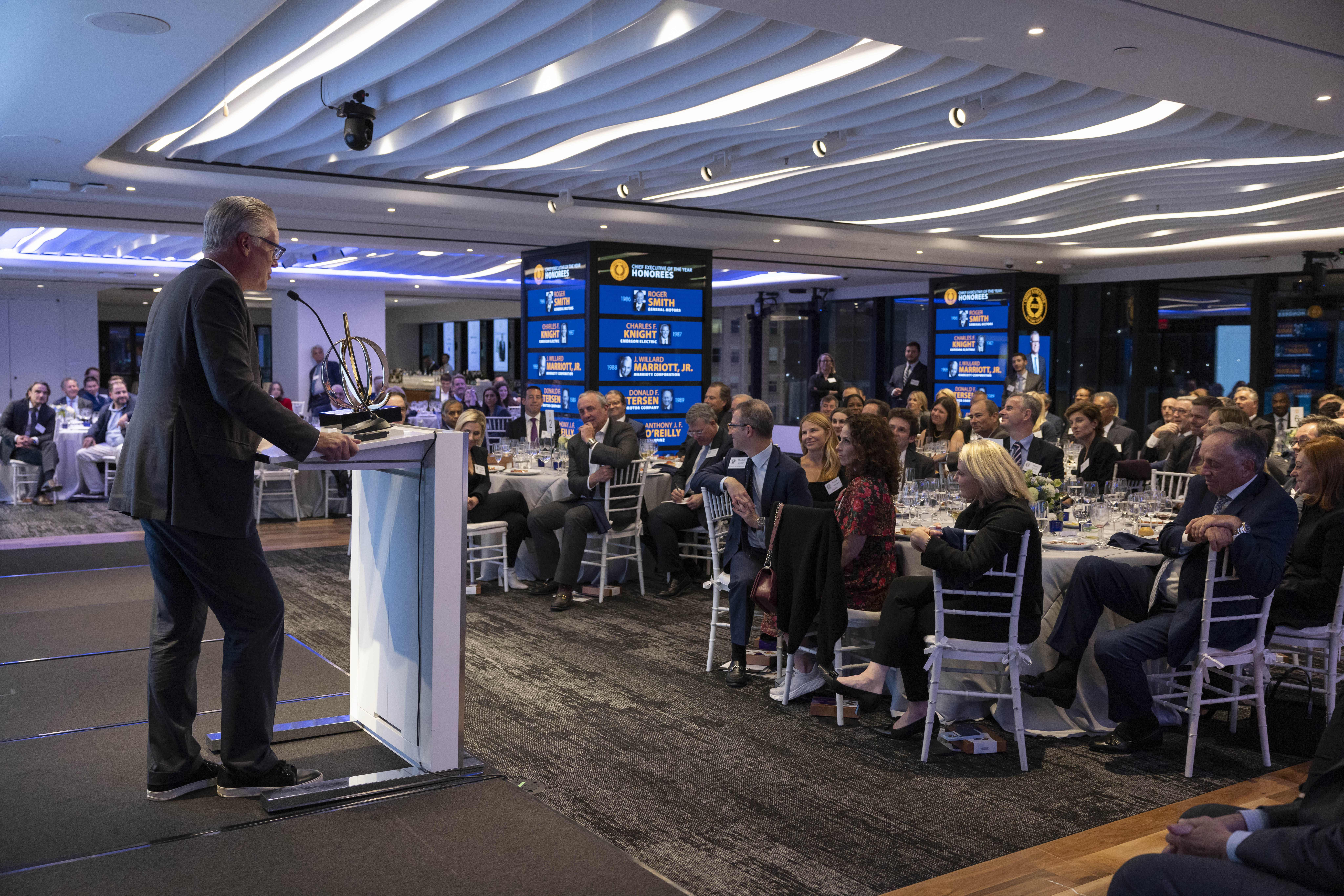 Ed Bastian stands at a podium and gives an acceptance speech to a room full of people seated at dining tables